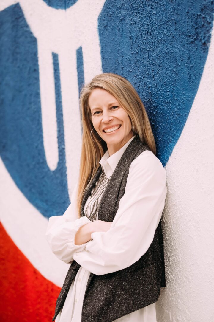 A woman standing in front of a wall with arms crossed.