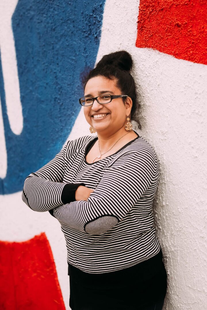 A woman standing in front of a wall with arms crossed.