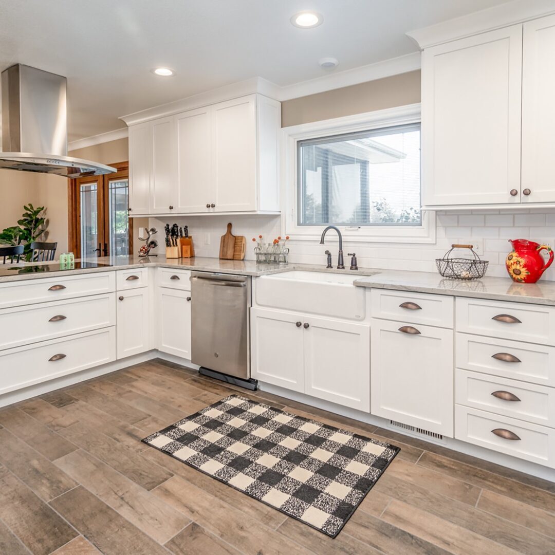 A kitchen with white cabinets and black checkered rug.